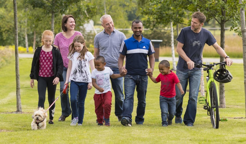 Group of people, including children and dogs walking through a park