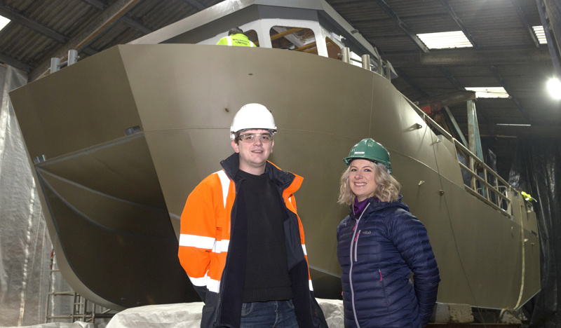 Two people standing in front of boat being constructed at Malakoff Limited, Shetland