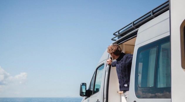 Man standing beside camper van admiring the view over blue sea