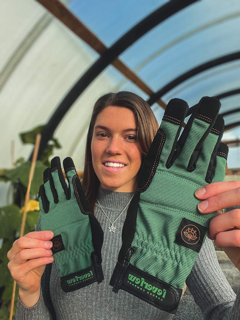 Woman holding up pair of green gloves in front of a greenhouse 